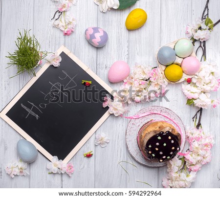 Easter cake with colored eggs and board chalk copy space on a white wooden background, top view flat lay