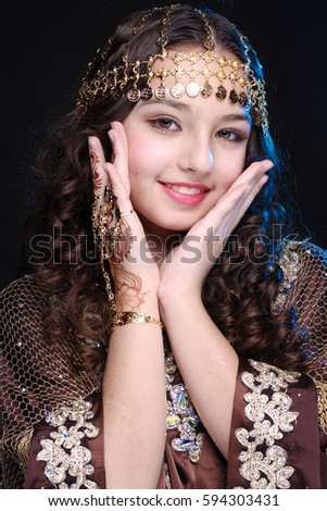 portrait of a young girl with long hair in oriental dancer costume Khaleej posing and dancing on a black background in the scenic blue light