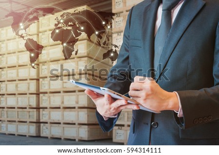 Businessman touching tablet for analyze stock at logistics port with blurred cargo warehouse background, transportation trading business concept, world map element of this image furnished by NASA