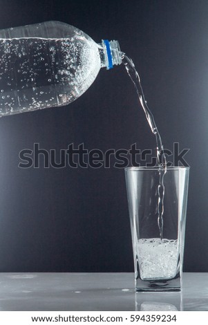 Bottle of clear drinking cold mineral water with gas in isolation on the background next to a glass transparent glass