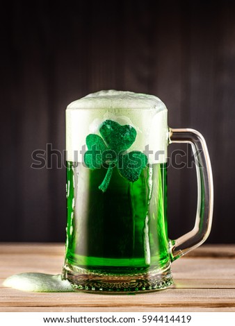 A glass of green beer adorned with clover on a beautiful wooden background
