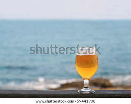 One glass of beer against sea and coastline a lot of space for text. Glas of beer on wooden fence of beach bar. Copy-space. Relaxation Concept. A Lot of Space for Text.