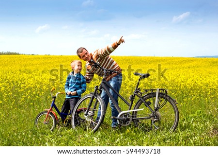 Father and son with bikes on country field with flowers in sunny day in spring
