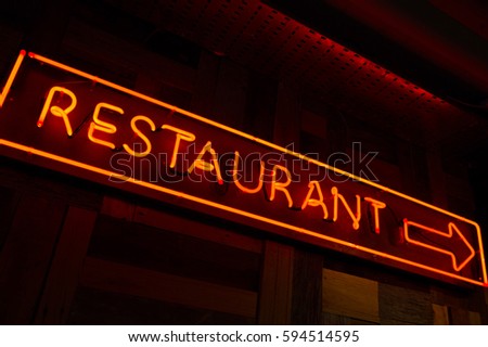 Lighted restaurant sign with arrow made of red fluorescent light in the wall with dark background