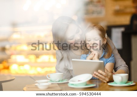 Woman showing her daughter interesting cartoon in touchpad while sitting in cafe