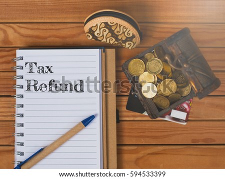 Business Concept. A box of coins, small purse and note book over the wood written TAX REFUND.