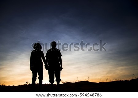 Silhouettes of lovers men and women stand on the background of sunset sky