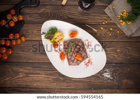 Beef steak in white plate on wooden table top. Top view. Rustic style. 