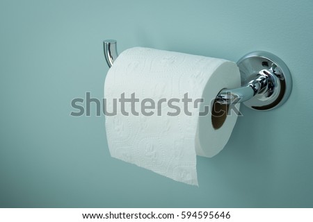 A white roll of soft toilet paper neatly hanging on a modern chrome holder on a light blue bathroom wall. Royalty-Free Stock Photo #594595646