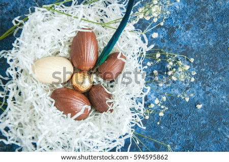 Chocolate Eggs in a nest with bird feathers on a blue textured background. Easter concept.
