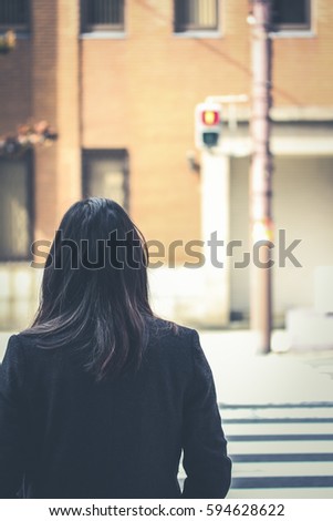 Girl waiting to cross the road with the pedestrian traffic lights show red sign