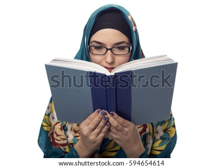 Female foreign exchange student wearing glasses and a hijab reading a text book.  The conservative outfit is associated with muslims or middle eastern and east european culture.