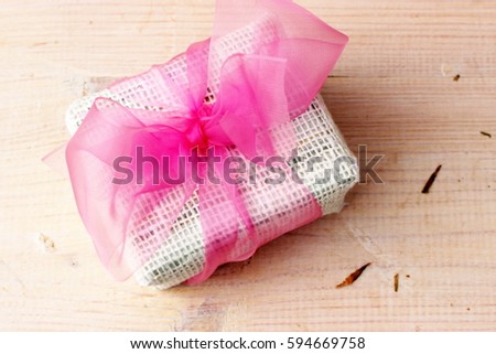 Very amazing small gift box wrapped with natural white cloth and decorated with beautiful pink ribbon with great pretty bow on white wooden background. Idea for girl or woman greeting