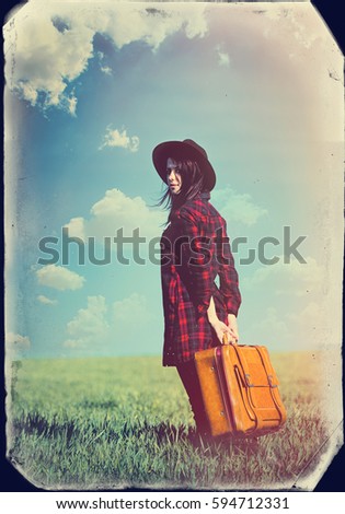 beautiful young woman with brown suitcase standing on the wonderful field background