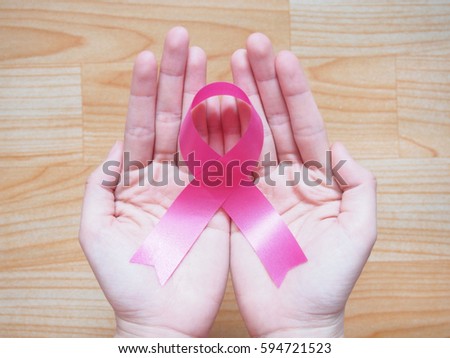 Closeup of human hand holding satin pink ribbon on wood background. Symbol is used to raise awareness for breast cancer, birth parents, nursing mothers and BRA. Women's healthcare and medical concept.