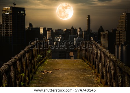 Old concrete bridge with wooden across to skyscrapers with super moon background at night. Dark tone and high contrast style. Sepia tone. The moon were NOT furnished by NASA.