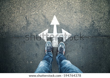 Business person standing at a crossroads. Conceptual business decision background. Point of view perspective used. Royalty-Free Stock Photo #594764378