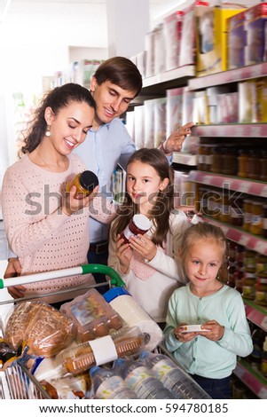 Positive couple with small kids  purchasing jam in hypermarket and smiling. Focus on girl
