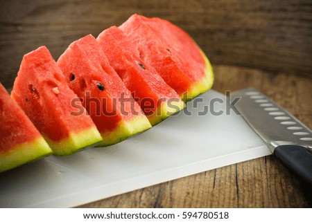 Watermelon slices on white plastic block with knife on wooden background