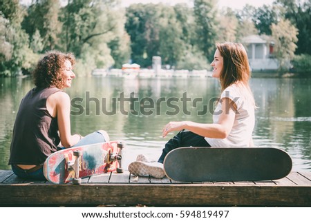 Two young girls enjoy skateboarding in the park in summer. Active live and sport concept. Toned picture