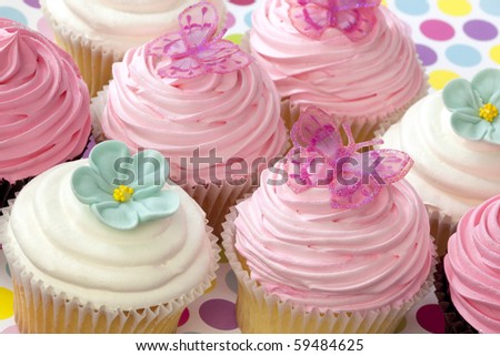 Lots of fancy cupcakes.  Frosted in pink and white, and topped with flowers and butterflies.  Pastel tones.