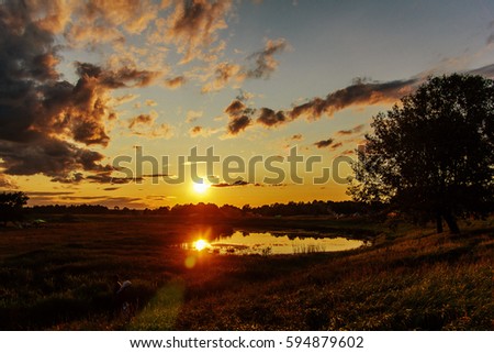 Beautiful small lake at sunset with reflection of clouds and sun on the background of wood. Russian nature.