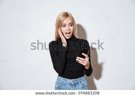 Photo of surprised young woman looking at mobile phone in her hand isolated on a white background