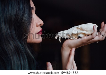 Portrait of a mysterious young girl holding a skull in the hands of a fox. Painted long hair jewelry rings on the fingers. Close-up. Closed eyes. Young witch before Halloween , bohemian.