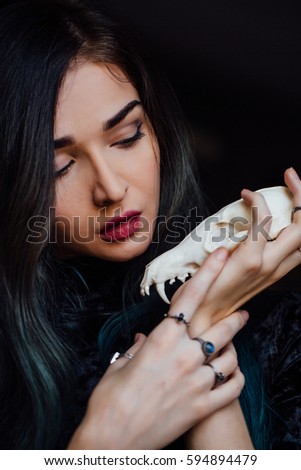Portrait of a mysterious young girl holding a skull in the hands of a fox. Painted long hair jewelry rings on the fingers. Close-up. Closed eyes. Young witch before Halloween , bohemian.