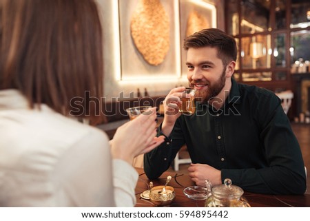 Photo of attractive young loving couple sitting in cafe and looking at each other.