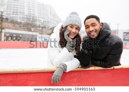 Photo of young happy loving couple skating at ice rink outdoors. Looking at camera.
