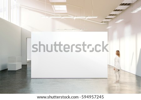 Woman walking near blank white wall mockup in modern gallery. Girl admires a clear big stand mock up in museum with contemporary art exhibitions. Large hall interior, banner exposition show