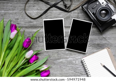 vintage retro camera with blank photo frames, blank notebook and tulip flowers bouquet on rustic wooden background. top view