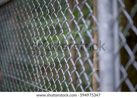 Close-up angle photograph of the chain links of a metal fence, with forest trees in the background. Border security and industry concept.