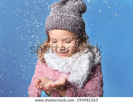 Cute little girl in warm clothes playing with snow on color background