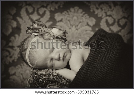 A small baby girl is having her first photo shoot. She is having a ribbon on her head and is covered with a black blanket. Black-and-white photography.