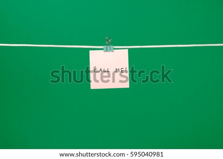 Pink paper note on the string with text Call Me! over colorful background