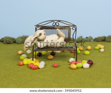 The Easter bunny takes a break from his preparations for Easter. He is laying on a bench surrounded by jelly beans.