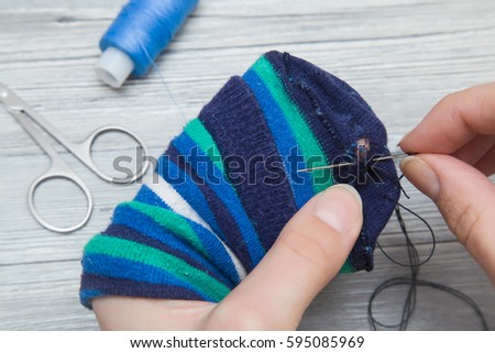 Hand with a needle and thread darning a sock. Handmade. Royalty-Free Stock Photo #595085969