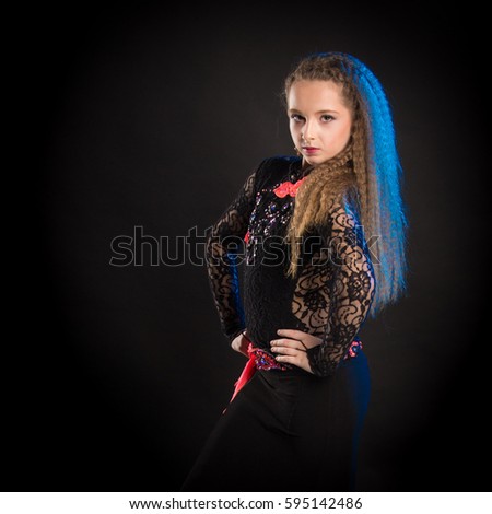 Portrait of a young girl with long hair in a black lace suit of a dancer posing on a black background in a scenic blue light