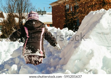 Funny little girl in a warm winter outfit, building a snow man. Kid playing outdoors in winter. Happy little kid is playing in snow, good winter weather. Child building snowman.