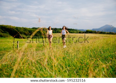 Funny female friends running in a meadow in summer. Focus on the grass, girls out of focus