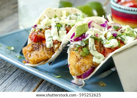 Close up of plate of fish tacos with salsa, avocado, coleslaw and lime creme sitting on blue plate