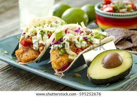 Fish tacos with fresh coleslaw, salsa, lime sour cream and avocado sitting on blue plate