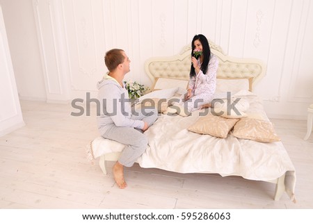 Thoughtful guy brought flower to girl bed for Good morning. Husband, wife sitting in bed. Mom, Dad European appearance. Concept of happy family life, success entertainment, advertising of Hotels or