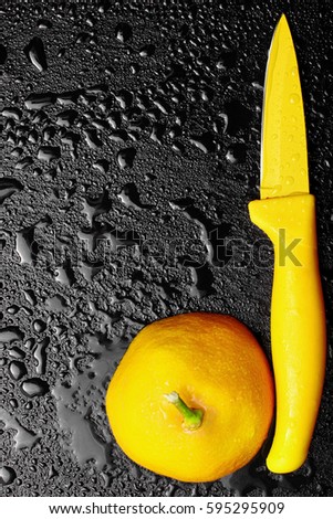 Slice of lemon with yellow knife on wet slate plate wiht a lot of water drops.Copy space .Top view