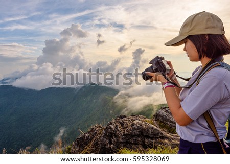 Hiker asian teens girl wear caps looking photo on digital camera is beautiful landscape natural of sierra and sky during sunset on mountain at Phu Chi Fa Forest Park, Chiang Rai, Thailand