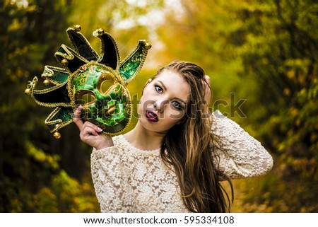 Beautiful woman in green carnival mask with metal bells . against autumn forest park background.Fall trees blurred backdrop Idea duplicity double game sham pretense hypocrisy postiche dissimulation