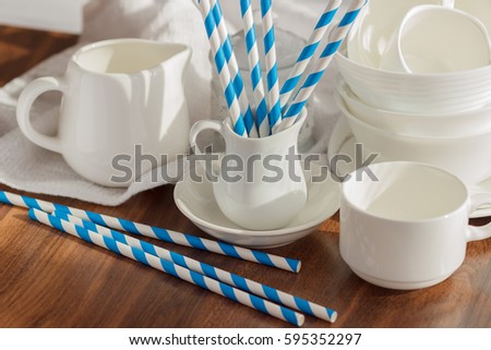 Set of white empty tableware with striped tubules, wooden background