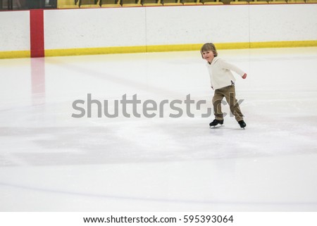 Little boy learning how to skate on indoor ice skating rink.